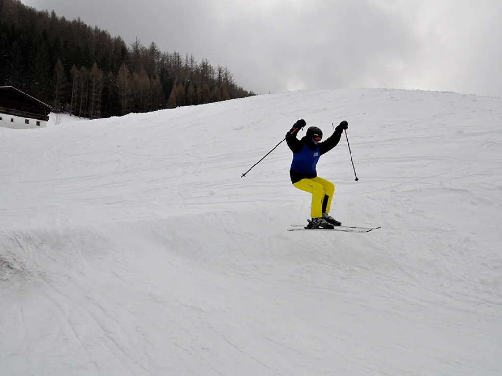 Skifahrer in gelber Hose hebt die Arme auf der Piste.